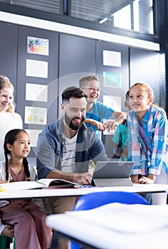 Vertical of happy diverse elementary children and male teacher using tablet in class, copy space