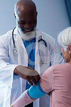 Vertical of happy diverse senior male doctor taking blood pressure of female patient, copy space
