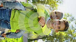 Vertical: Happy little boy riding brother's back at park, smiling to camera