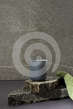 Vertical iamge.Aroma candle on the stack of marble pieces, green towel against grey wall.Concept of bath relaxation