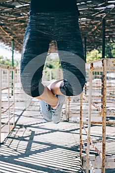 Vertical image of an athletic young woman doing pull-ups outdoor