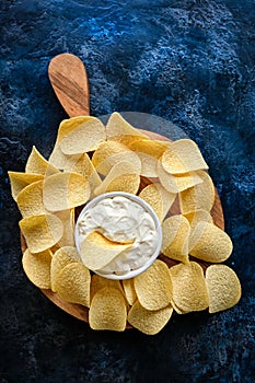 Vertical image beautiful potato chips and sauce in a white bowl on a wooden cutting board