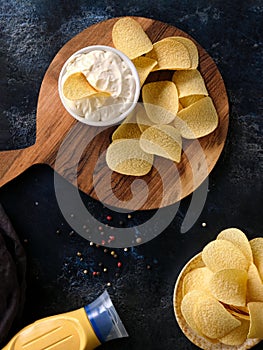 Vertical image beautiful potato chips and sauce in a white bowl on a wooden cutting board