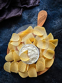 Vertical image beautiful potato chips and sauce in a white bowl on a wooden cutting board