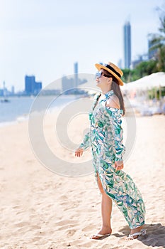 Vertical image. Beautiful woman standing relaxing on the beach. Summer time. Happy person wearing sunglasses and brown straw Hats