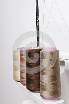 Vertical image.Beige colors of spools of thread, overlock machine for sewing against white background photo