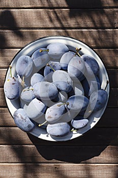 Vertical image.Bowl of juicy tasty plums in the bowl on the wooden brown table