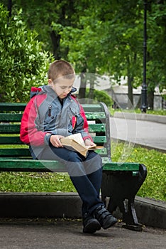 Vertical image of boy reading a book on bench