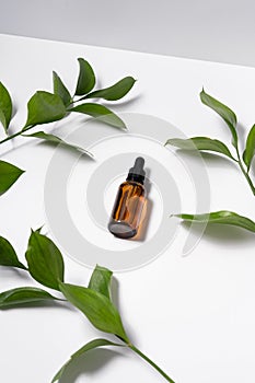 Vertical image of a brown bottle of natural serum lies on a white background with plant leaves. Protector skin, treatment facial photo