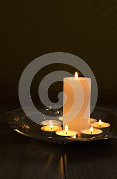Vertical image. Candles and candlelights. Golden salver and candles on it against brown background