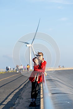 Vertical image of Caucasian waman with sunglasses stand in front of wind turbine or windmill also look to left side near the road