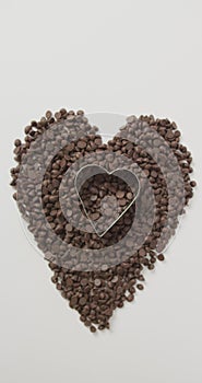 Vertical image of chocolate chips forming heart with heart shaped cookie cutter on white background