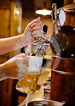 Vertical image close up view female barman hands pouring beer in mug