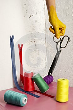 Vertical image.Colored woman hand, scissors, assortment of different colors of thread,zippers on the pink surface against white wa