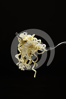 Vertical image.Delicious cooked noodles on the fork against black background