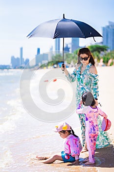 Vertical image. Family travel at the sea and beach. Aunt and granddaughters playing by seaside. Woman holding black umbrella