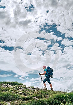 Vertical image of female backpacker climbing to the mountain top using trekking poles with bright cloudscape background. Active