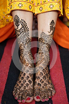 Vertical image of a female feet in yellow dress with wedding henna decorations