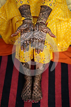 Vertical image of a female in yellow dress showing wedding henna decorations on hands and feet