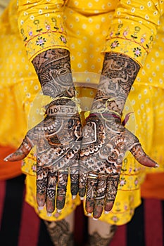 Vertical image of a female in yellow dress showing wedding henna decorations on hands and feet