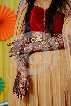 Vertical image of a female in yellow dress showing wedding henna decorations on hands and feet