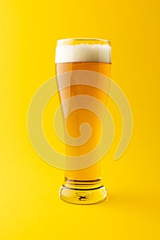 Vertical image of full pint glass of lager beer on yellow background, with copy space