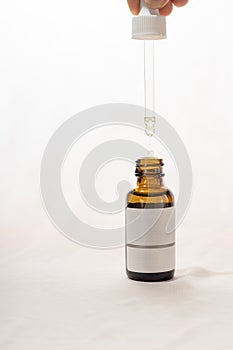 Vertical image of glass bottle with blank label and pipette,oil drops against white background