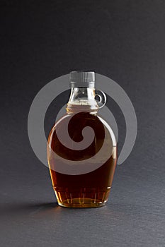 Vertical image of glass bottle of maple syrup on dark grey background, with copy space