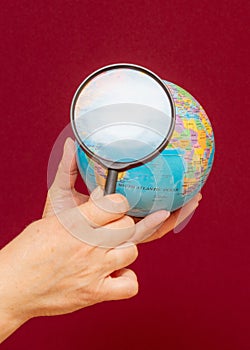 Vertical image of a hand holding a magnifying glass over an world globe