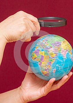 Vertical image of a hand holding a magnifying glass over an world globe