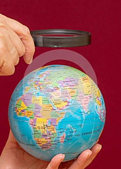 Vertical image of a hand holding a magnifying glass over an world globe