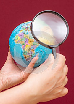 Vertical image of a hand holding a magnifying glass over an world globe