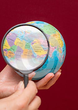 Vertical image of a hand holding a magnifying glass over an world globe