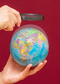 Vertical image of a hand holding a magnifying glass over an world globe