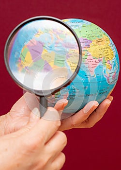 Vertical image of a hand holding a magnifying glass over an world globe