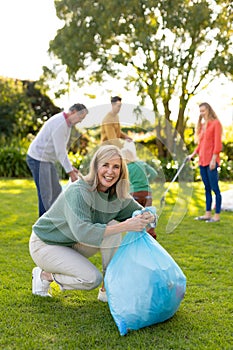 Vertical image of happy caucasian woman with rubbish bags in garden