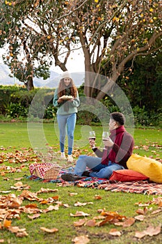Vertical image of happy diverse couple having picnic in autumn park