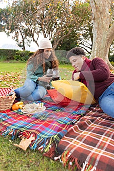 Vertical image of happy diverse couple having picnic in autumn park