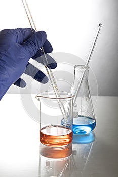 Vertical image of lab assistent who holding glass pipette,two glass flasks on the table