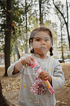 Vertical image of a little girl with a bottle of soap bubbles toy in a park