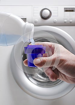 Vertical image.Man holding a cup and pouring liquid laundry detergent against washing machine.Household routine