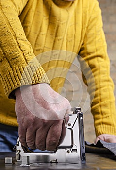 Vertical image.Man using metal staple gun and fixing furniture