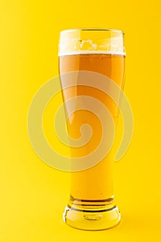 Vertical image of nearly full pint glass of lager beer on yellow background, with copy space