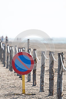 Vertical image of a no parking traffic sign on a beach with a wooden log fence attached with a rope