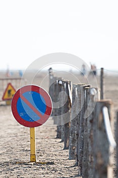 Vertical image of a no parking traffic sign on a beach with a wooden log fence attached with a rope