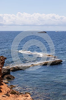 Vertical image of part of the coastal cliff smoothly disappearing underwater, light ripples on sea in Ibiza