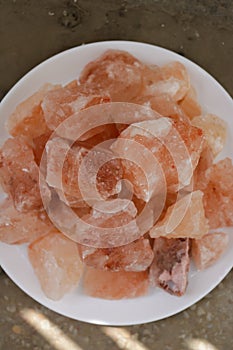 Vertical image of pink himalayan salt pieces on a white plate.