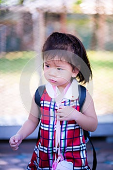 Vertical image. Portrait of 2-3 years old baby. Asian girl stood and frowned. She grasped the strap of the drinking water bottle.