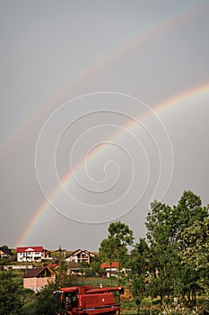 Vertical image of a rainbow above a village with trees and against a hazy sky