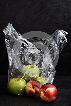 Vertical image of ripe apples and nectarins in transparent plastic bag on black background